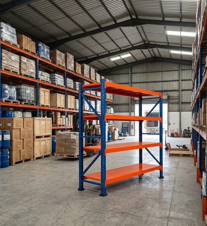 A four-tier warehouse shelving unit with blue vertical supports and orange horizontal beams, positioned in a large industrial warehouse with other shelving and stacked boxes in the background.